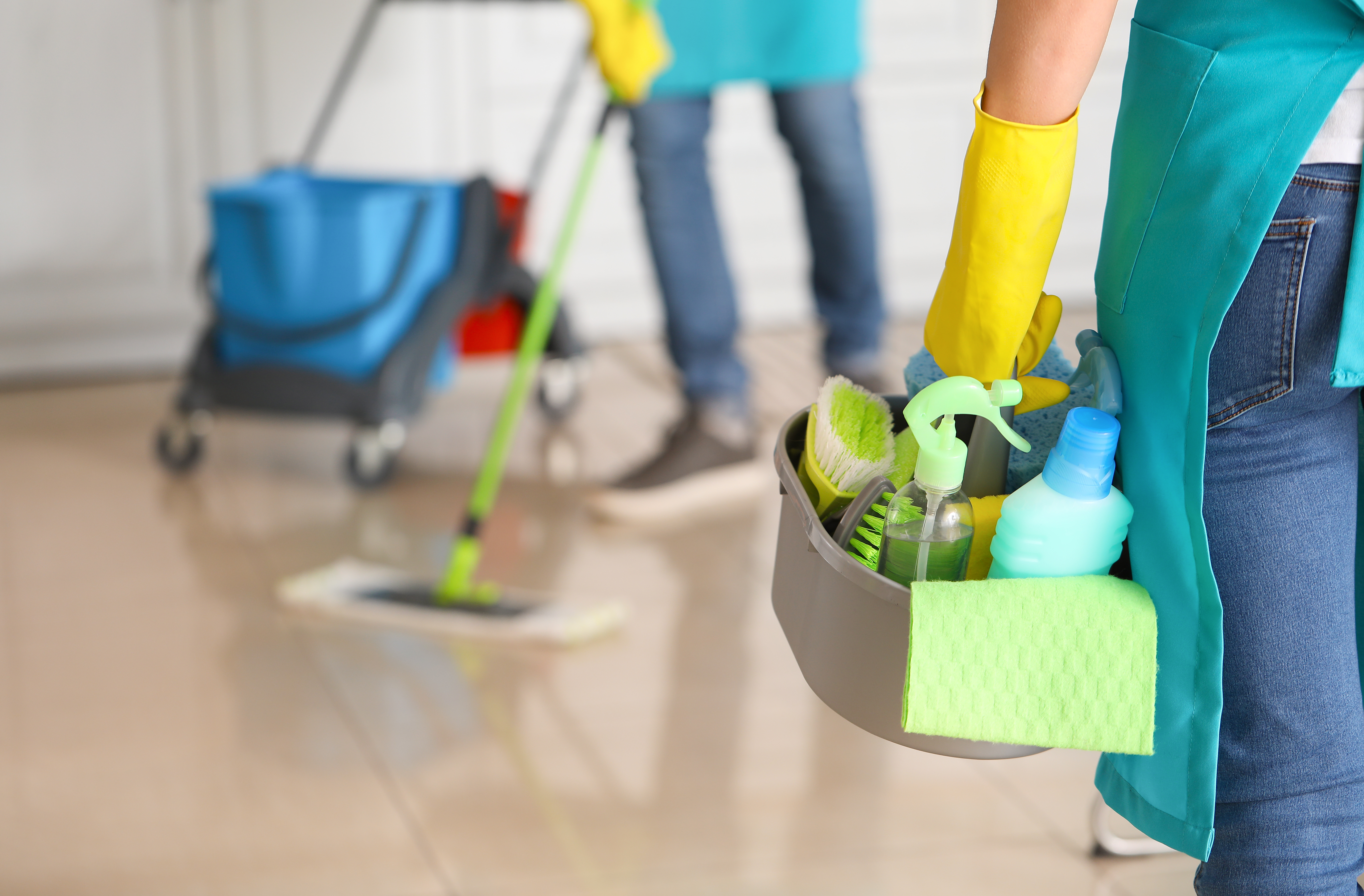 Professional cleaner holding caddy with supplies and mop while team works in background