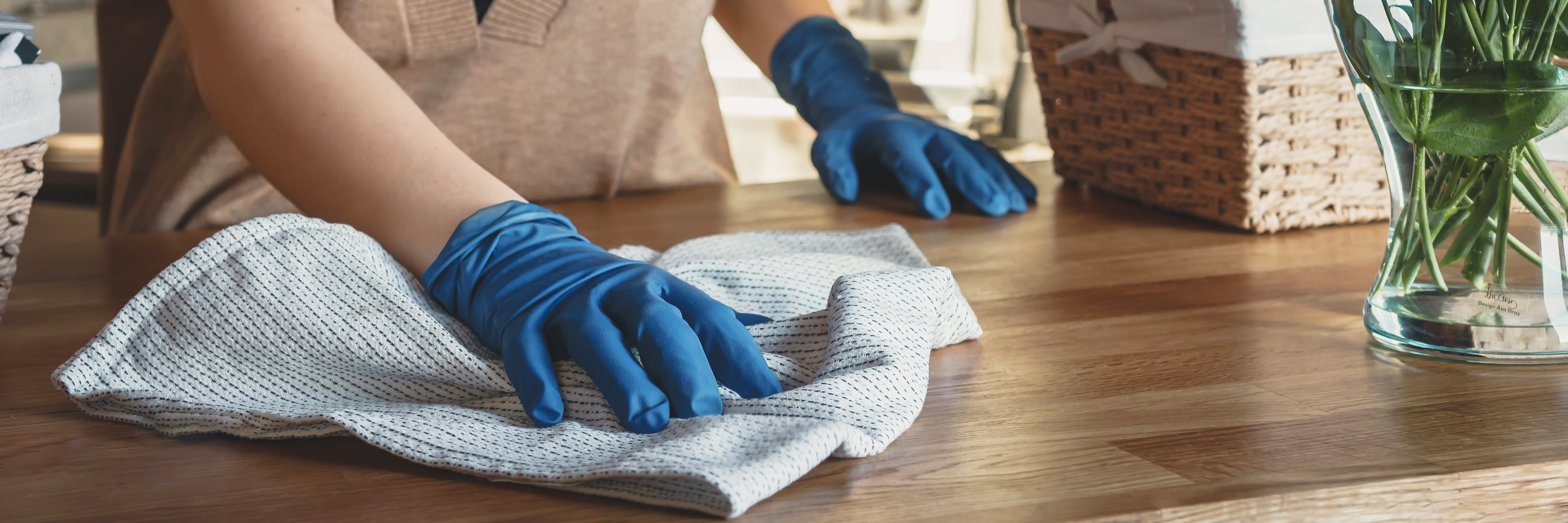Person wearing blue gloves cleaning wooden table with microfiber cloth