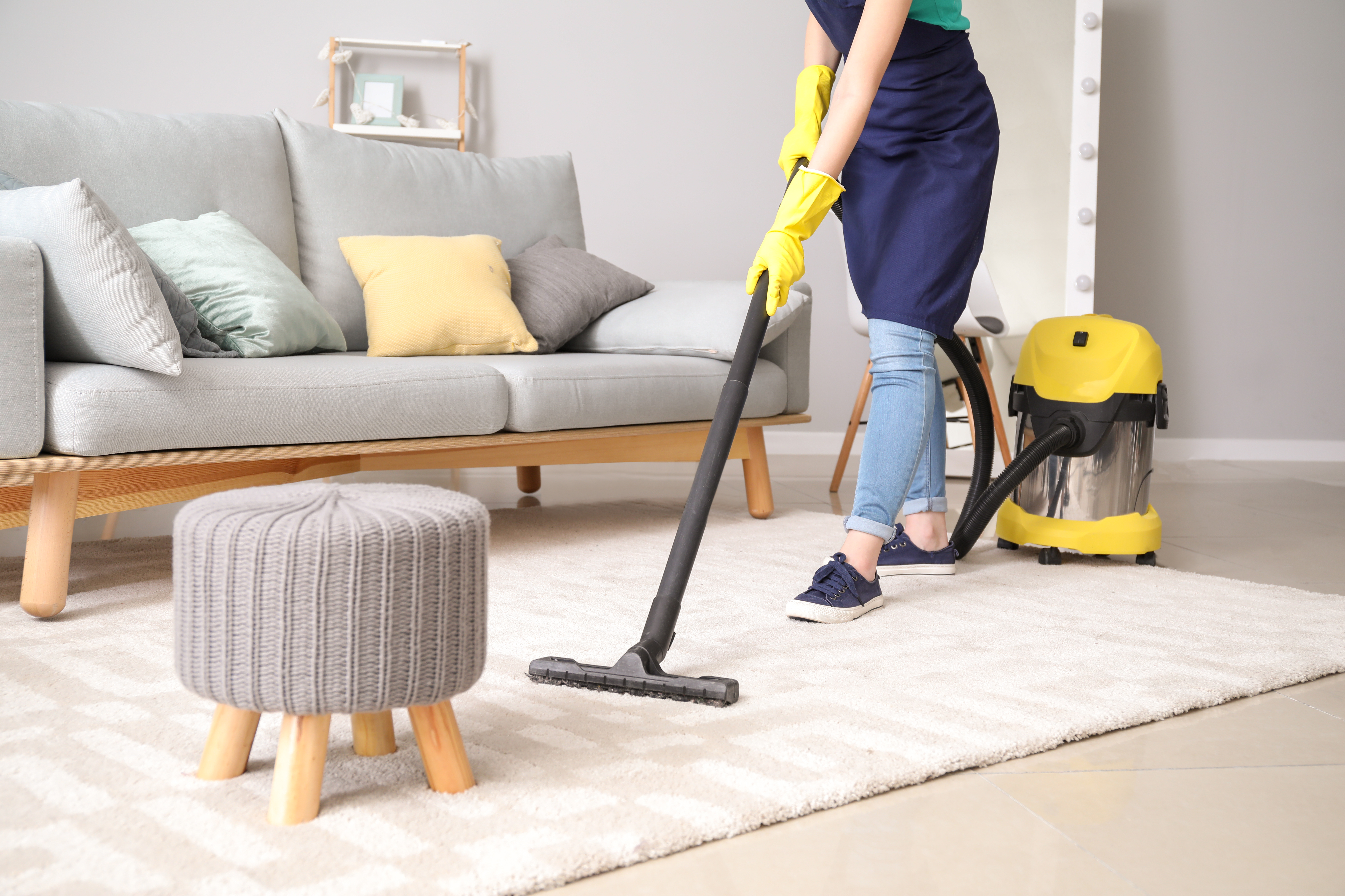 Person vacuuming living room carpet with yellow and black wet-dry vacuum cleaner